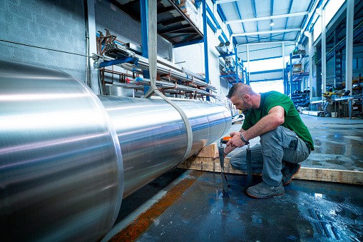 Industrial worker moving with crane big stainelss steel pipes