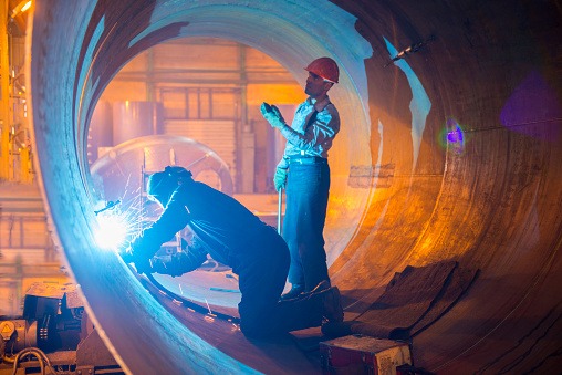 Two welders work in a pipe for an oil pipeline.